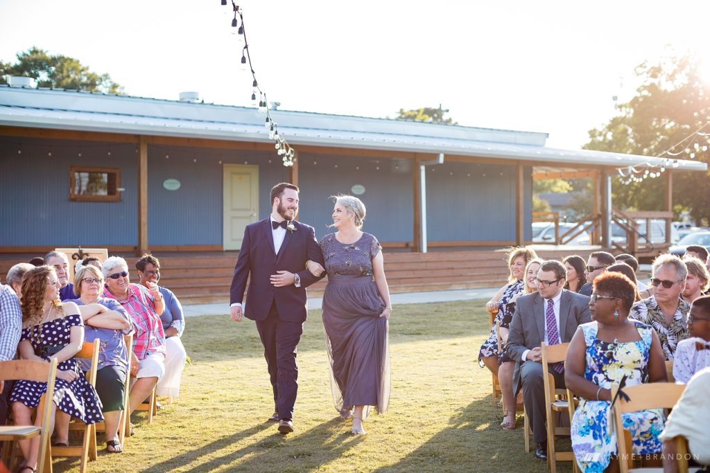 Groom escorts his mother down the aisle at outdoor wedding at Warehouse 535